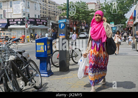 Une femme musulmane dans un hijab & robe traditionnelle marche sur 74e St. à Jackson Heights, Queens tout en discutant avec son téléphone portable. Banque D'Images