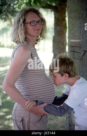 Frère aîné avec maman enceinte hugging bump Banque D'Images