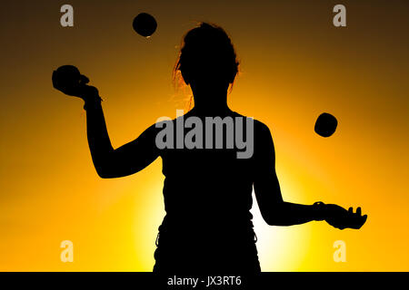 Silhouette d'une femme à jongler avec des balles sur le coucher du soleil Banque D'Images