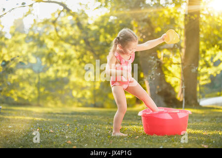 La jolie petite fille blonde jouant avec les projections d'eau sur le terrain en été Banque D'Images