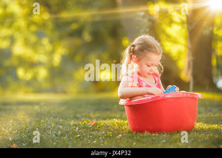 La jolie petite fille blonde jouant avec les projections d'eau sur le terrain en été Banque D'Images