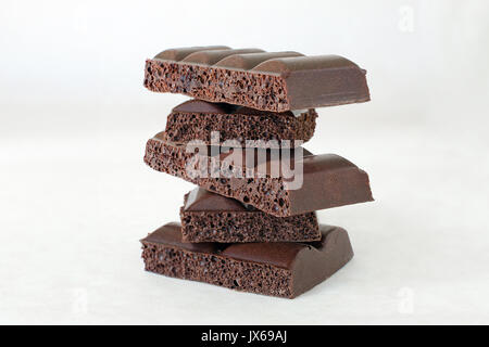 Morceaux de chocolat noir poreux empilés sur un fond clair Banque D'Images