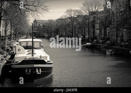 Bateau amarré dans un canal à Amsterdam (Pays-Bas). Mars 2015. Le format paysage. Version noir et blanc. Banque D'Images