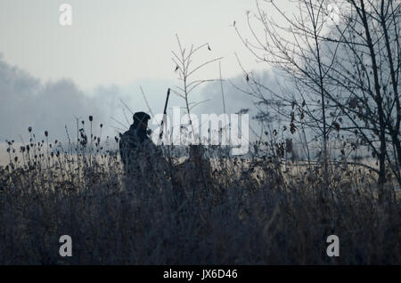 La silhouette de deux chasseurs au lever du soleil. Hunter man and boy pendant la période de chasse à la recherche de gibier ou de jeu. Automne saison de chasse. T grand-père Banque D'Images