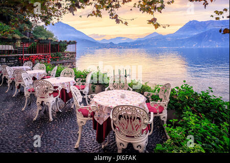 Les tables d'un petit café au bord du Lac de Côme, Italie, avec panorama des alpes montagnes en arrière-plan sur le coucher du soleil Banque D'Images