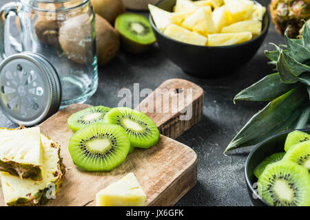 Kiwi et d'ananas frais tranchés sur planche de bois sur fond sombre. Ingrédients smoothie Banque D'Images