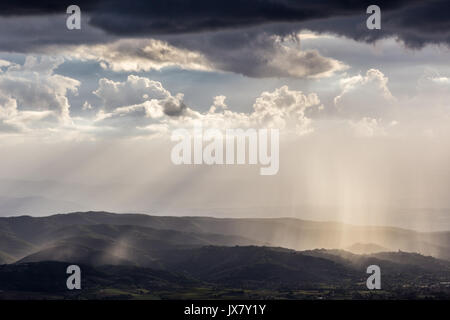 Vue spectaculaire sur les rayons du soleil et de la pluie sur certaines montagnes et collines, un benath moody et ciel nuageux Banque D'Images