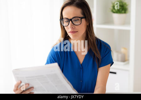 Femme dans les verres reading newspaper at office Banque D'Images