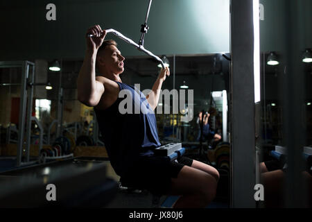 Man flexing muscles sur le câble de la machine en salle de sport Banque D'Images