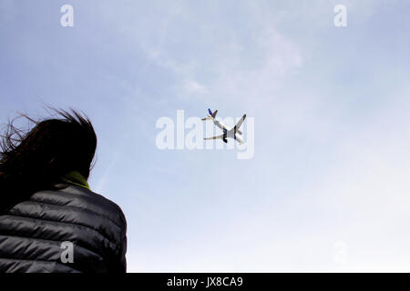 Une jeune femme aux cheveux noirs regarde un avion qu'il s'apprête à atterrir. Banque D'Images