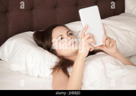 Young woman holding digital tablet au lit, lecture d'e-book Banque D'Images