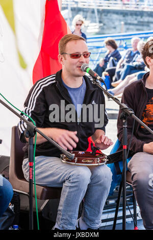 Jeune homme de race blanche, 20 ans, assis à l'extérieur, singing into microphone et jouant du tambourin. Membre du groupe de musique Samba Azul. Banque D'Images