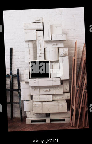 Un grand nombre de valises blanc de formes différentes sont empilés les uns sur les autres et une photo sous la forme d'un rectangle noir, contre un mur en brique blanche Banque D'Images