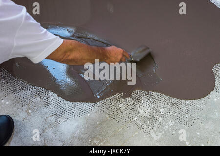 Worker met une chape d'auto-nivellement sur plancher de béton. Vacances en construction Banque D'Images