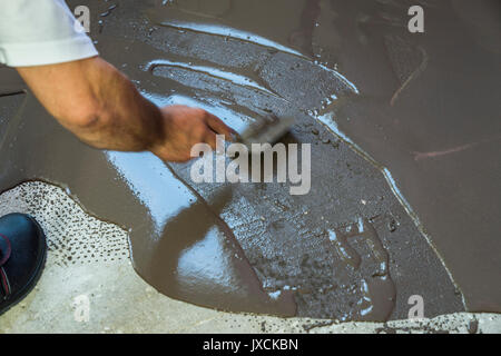 Worker met une chape d'auto-nivellement sur plancher de béton. Maison en construction Banque D'Images