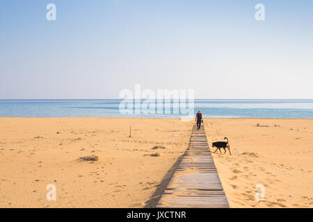 Homme avec chien marcher sur le chemin en bois sur la plage et à la recherche dans la distance de l'océan. Banque D'Images