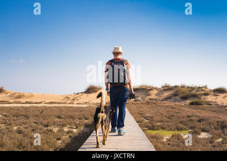 Homme avec chien marcher sur le chemin en bois sur la plage et à la recherche dans la distance de l'océan. Banque D'Images