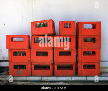 Bouteilles empilées dans des caisses en plastique rouge contre un mur blanc Banque D'Images
