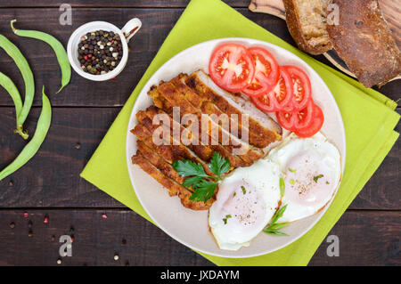 Morceaux de chop (schnitzel), pain grillé avec des oeufs, la tomate fraîche sur un fond de bois sombre. Vue d'en haut. Banque D'Images