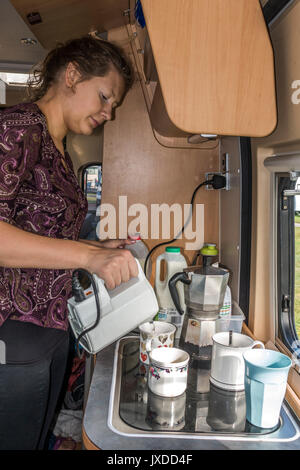 Jolie jeune femme faisant du thé dans un camping-car sur un terrain de camping. Exeter, Devon, Angleterre, Royaume-Uni. Banque D'Images