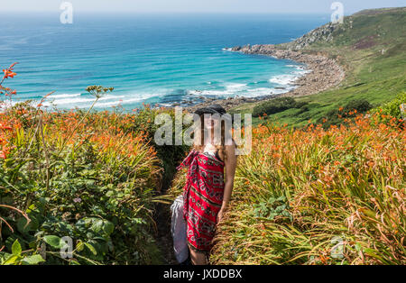 Une jolie jeune femme, portant un sarong et chapeau, debout sur un étroit sentier menant à Gwynver beach, Cornwall, England, UK. Banque D'Images