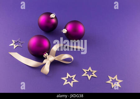 Belle pourpre des boules de noël avec effet satin, ruban cadeau gris et argent métallique étoiles sur fond violet. Banque D'Images