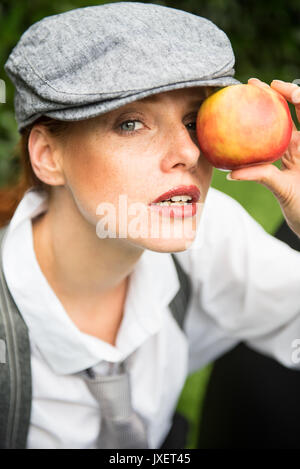 Red-haired woman with cap dans le jardin est titulaire d'Apple avant de l'œil Banque D'Images