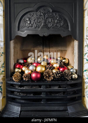 Jolie cheminée en fonte de style victorien et grille décorée de boules de Noël colorées et de cônes de sapin, Angleterre, Royaume-Uni Banque D'Images