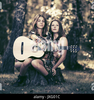 Deux filles de la mode avec la guitare dans une forêt d'été Banque D'Images