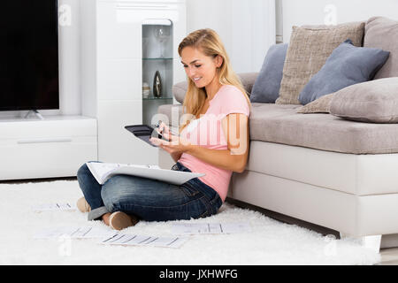 Young Smiling Woman Sitting on Calcul de facturer à l'aide de tapis calculatrice à la maison Banque D'Images