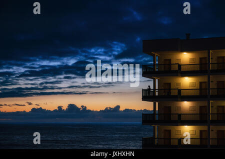Silhouette d'une femme se tient sur le balcon d'un grand bâtiment de l'hôtel et admirer le coucher de soleil sur la mer Banque D'Images