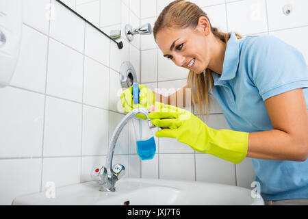 Jeune femme portant des gants Nettoyage du robinet du bassin à l'aide de pulvérisateur à bains Banque D'Images