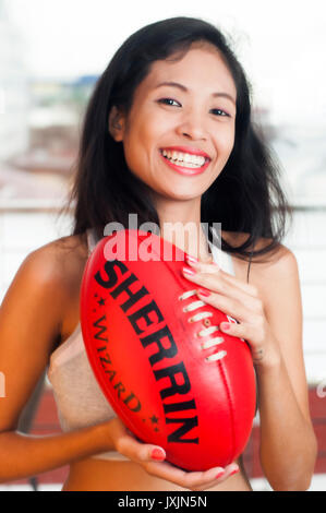 Young Asian woman holding Australian rules football AFL Banque D'Images