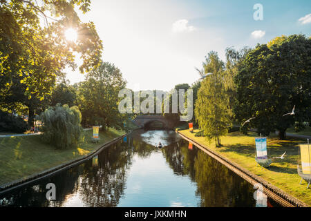 Riga, Lettonie. Ville Rivière Canal dans le parc de la colline Bastion. Soleil qui brille à travers les feuilles vertes sous le soleil de soir d'été. Fontaines dans l'eau de rivière Canal. Banque D'Images