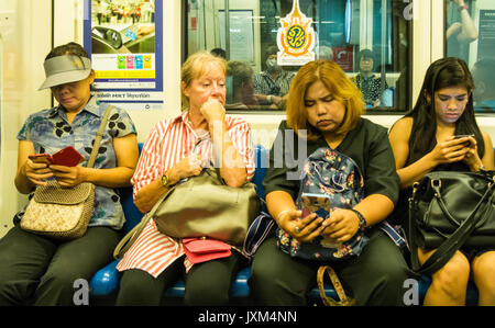 Hauts femme entourée par d'autres passagers sur des téléphones mobiles sur le MRT (Mass Rapid Transport) anglosaxon), Bangkok, Thaïlande Banque D'Images