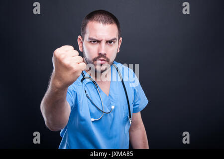 Docteur fou wearing scrubs avec stéthoscope montrant fist sur fond noir avec copypsace zone publicitaire Banque D'Images
