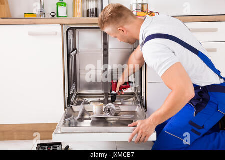 Jeune réparateur lave-vaisselle Fixation avec perceuse électrique Banque D'Images