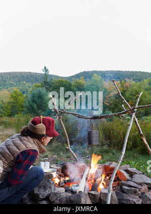 Femme assise à côté d'un feu de camp, la cuisson des aliments, Colgate, forêt sauvage du Lac Parc Catskill, New York State, USA Banque D'Images