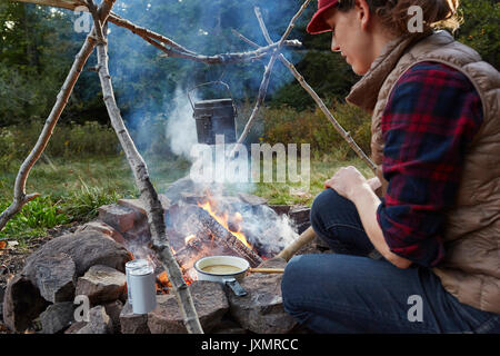 Femme assise à côté d'un feu de camp, la cuisson des aliments, Colgate, forêt sauvage du Lac Parc Catskill, New York State, USA Banque D'Images