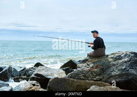 Jeune homme assis sur le roc de la pêche maritime Banque D'Images