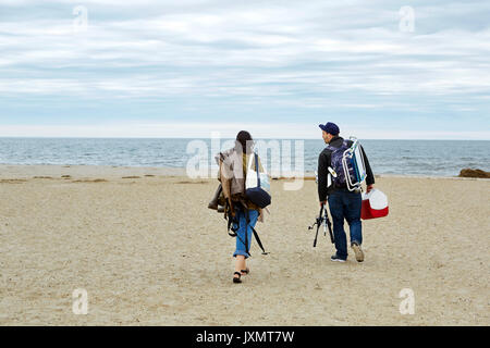 Vue arrière du jeune couple transportant du matériel de pêche en mer sur la plage Banque D'Images