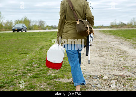 Jeune femme à marcher en direction de voiture, transportant la canne à pêche et attaquer fort, vue arrière Banque D'Images