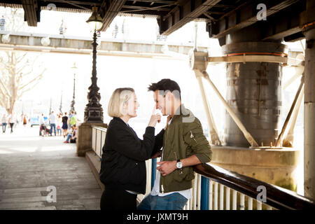 Jeune couple, debout sous pont, young woman touching man's face, smiling Banque D'Images