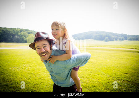 Portrait of mid adult man giving daughter un piggy back in rural field Banque D'Images