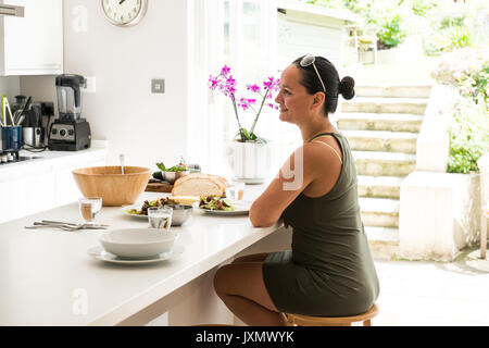 Femme assise à la cuisine île bénéficiant d'un déjeuner salade Banque D'Images