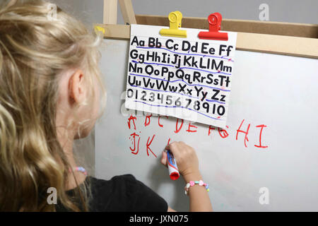 Petite fille pratiquer ses lettres sur un tableau effaçable à sec Banque D'Images