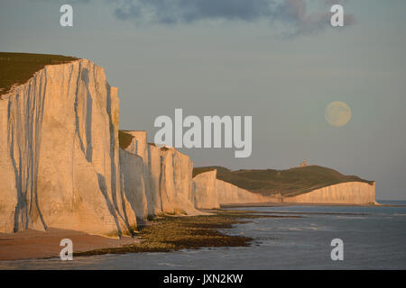 Lune croissante au sujet des sept Sœurs des falaises de craie au coucher du soleil. Banque D'Images