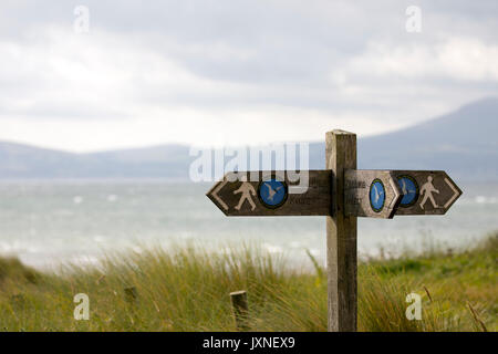 Direction en bois façon post montrant marqueur direction pour le pays de Galles chemin côtier à dunes sur Warrren Newborough Plage avec la mer et les collines au loin Banque D'Images