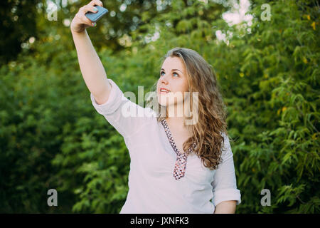 Belle jeune fille de race blanche assez grande taille Femme habillé en blouse blanche à profiter de la vie, sourire, s'amusant et en prenant des photos sur Smartphone Selfies Banque D'Images