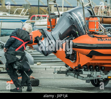 Un homme âgé en pressant une combinaison de plongée, à côté d'un bateau gonflable rigide (RIB) avec moteur hors-bord, sur une remorque, dans le port de Penzance, Banque D'Images